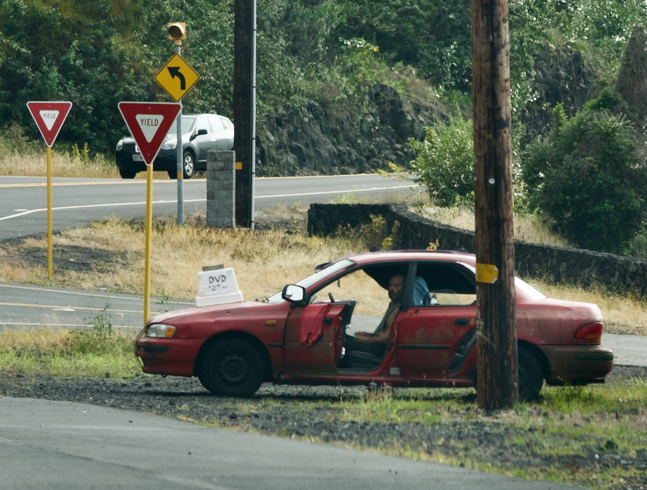 A guy sits in a car on the side of the road selling DVD's.